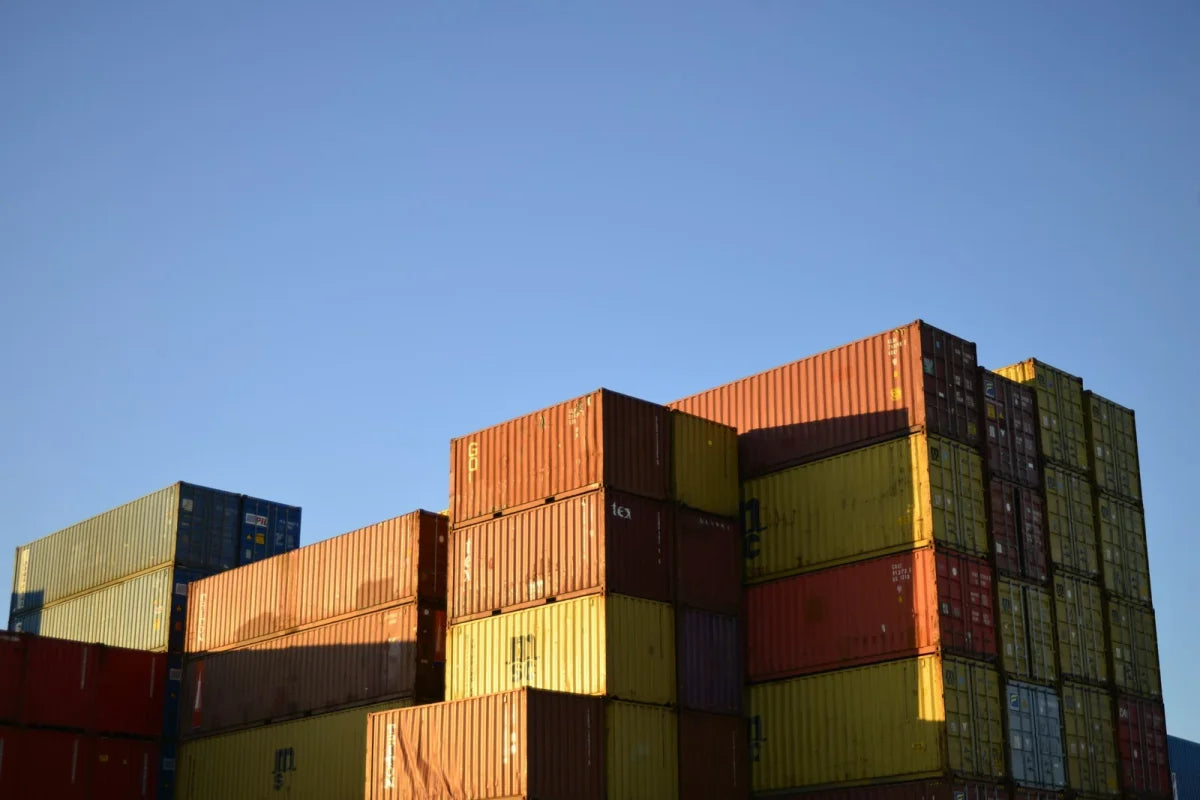 Orange, yellow and red shipping containers stacked in a quiet yard under a clear sky