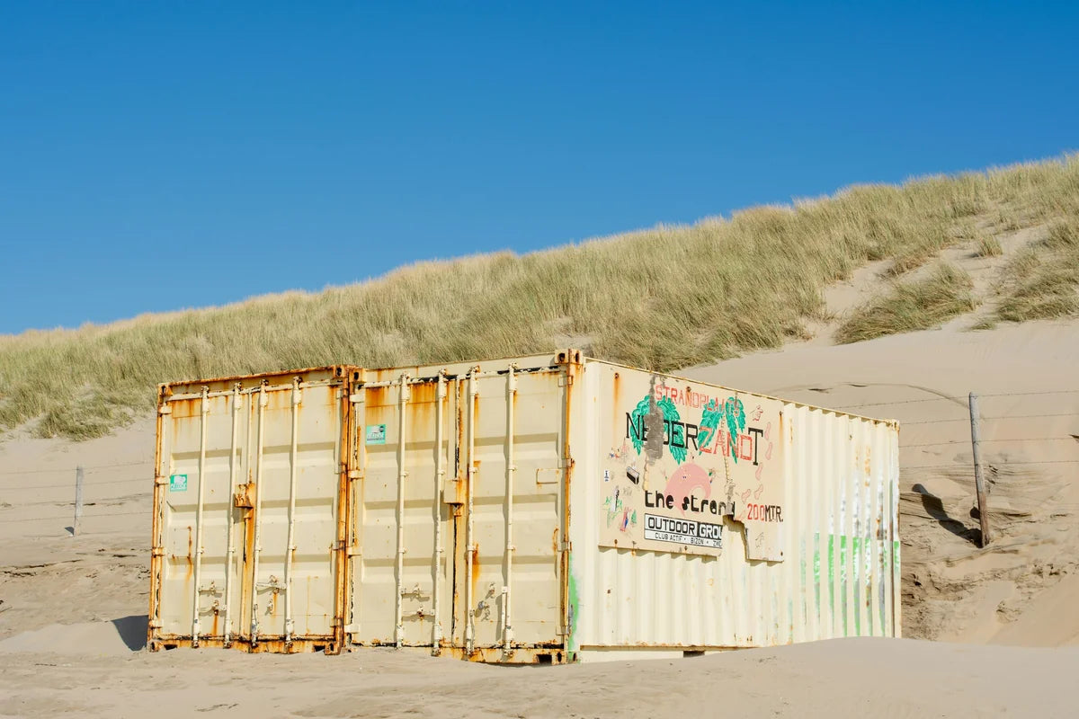 Weathered cream shipping container with rust streaks and patina sitting on sandy ground