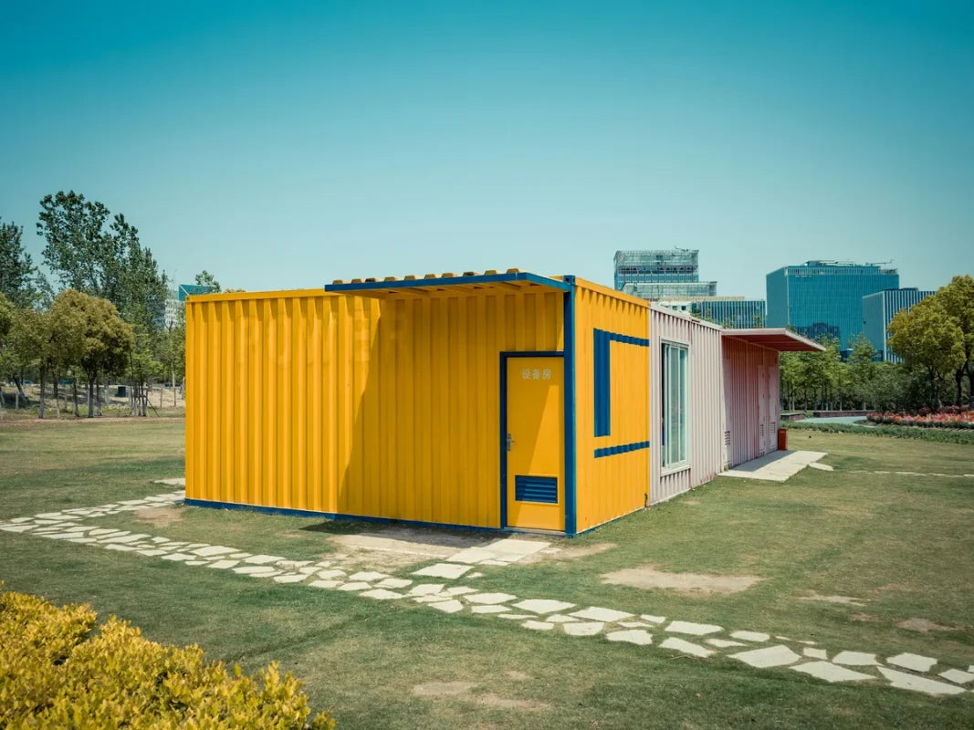Yellow modified shipping container building with a framed door and window on a lawn