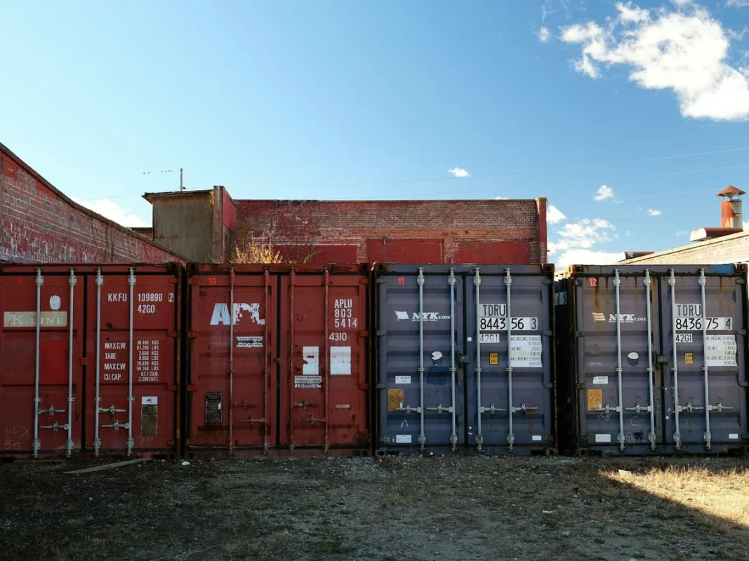 Row of used red and grey shipping containers lined up on a lot under a blue sky