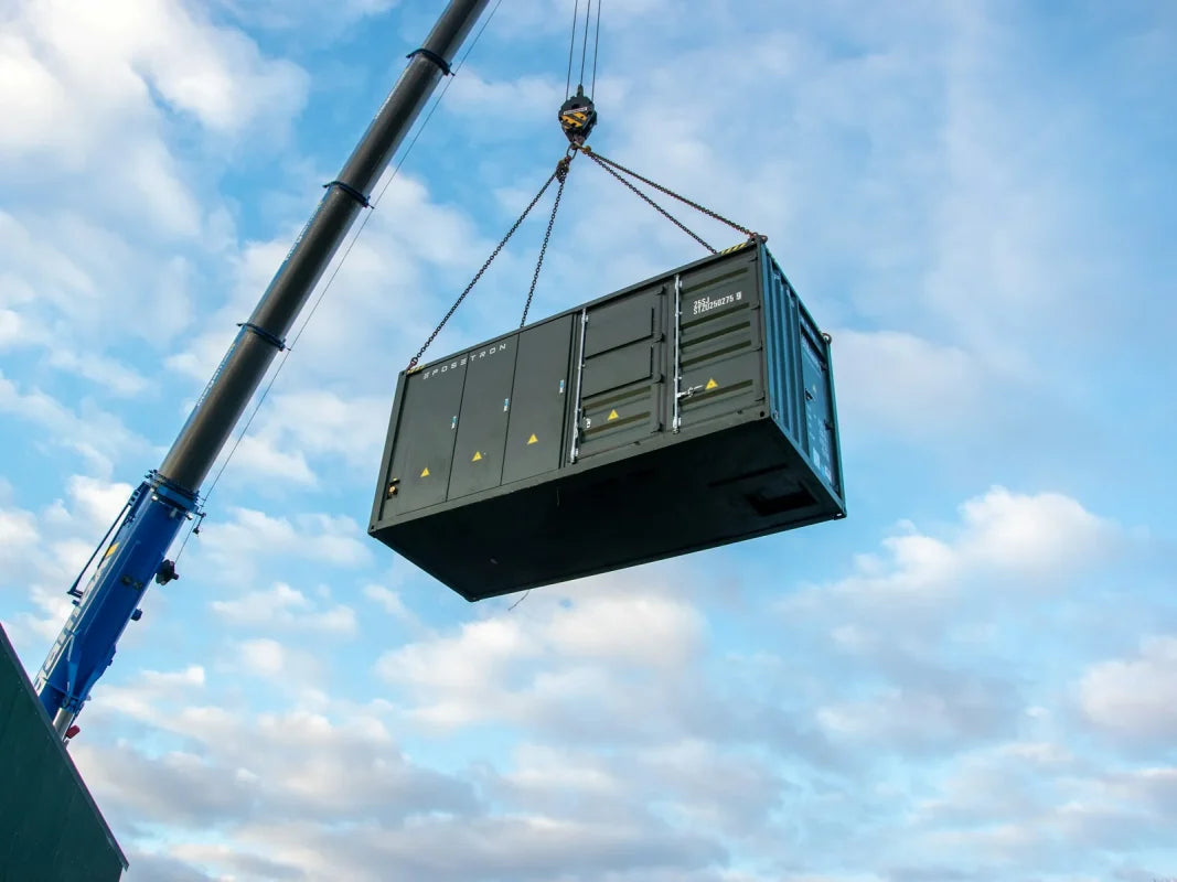 Mobile crane lifting a dark green shipping container into place against a cloudy sky